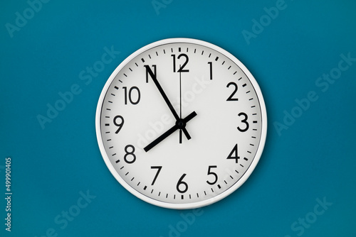 A white wall clock hangs on a blue wall with copy space and a central composition. photo