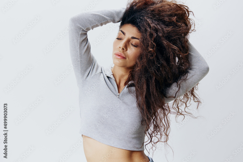 Love Yourself. Natural Curly Latin Female in Pastel Gray Sweater and Jeans Stroking Hair Closing Eyes, Posing Isolated At White Studio Wall Background. Fashion Seasonal Sale New Collection Concept Love Yourself. Natural Curly Latin Female in Pastel Gray Sweater and Jeans Stroking Hair Closing Eyes, Posing Isolated At White Studio Wall Background. Fashion Seasonal Sale New Collection Concept
