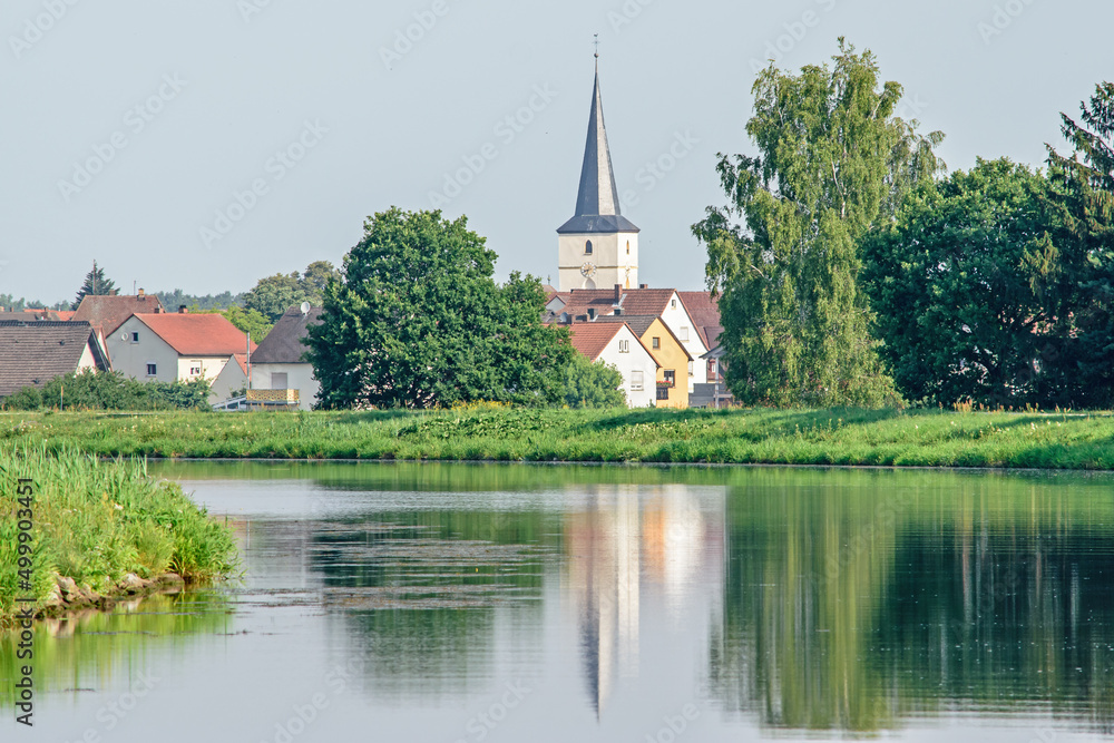A church spire reflects on the calm waters of a river in Germany.