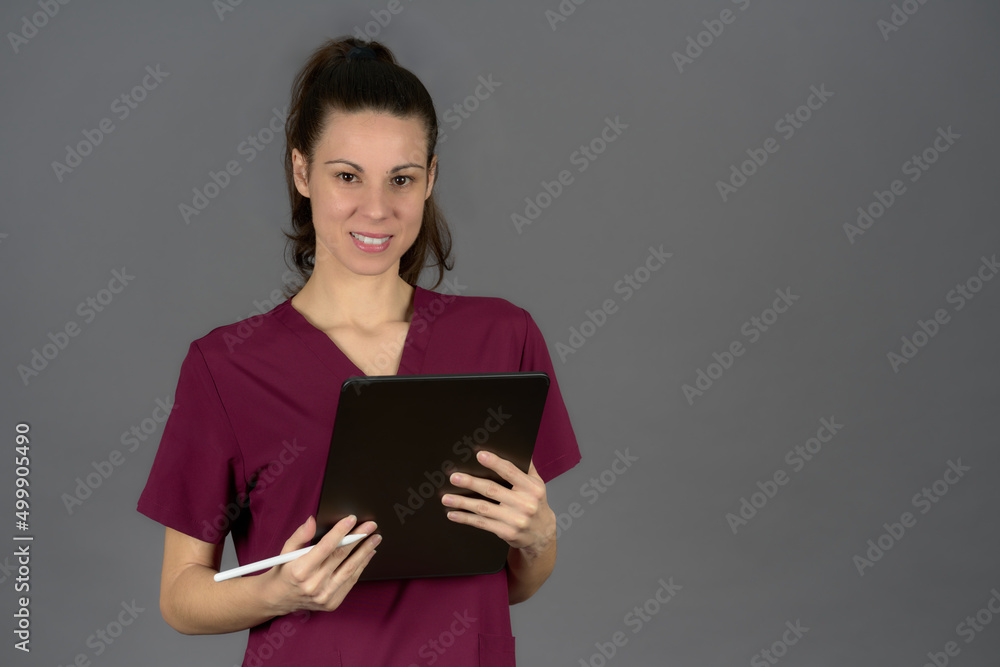 smiling female nurse in purple uniform looking at camera with digital tablet report on gray background smiling female nurse in purple uniform looking at camera with digital tablet report on gray background