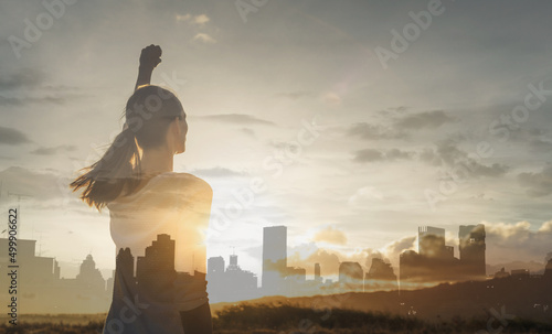 Modern day woman supper hero in the city. Strong young woman with fist In the sky facing the city sunset  photo