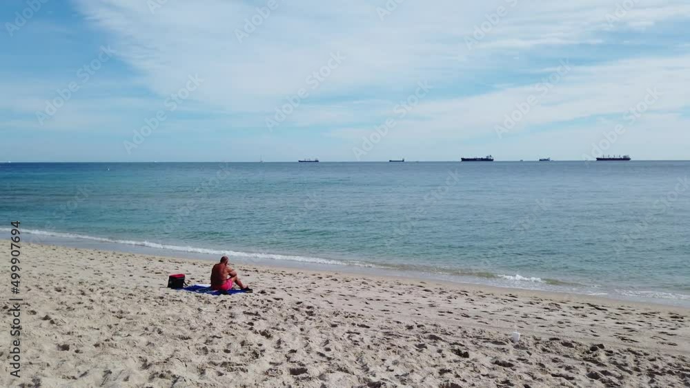 A unidentifiable old man sits on a deserted beach looking out at a row of tankers out in the calm ocean
A unidentifiable old man sits on a deserted beach looking out at a row of tankers out in the calm ocean