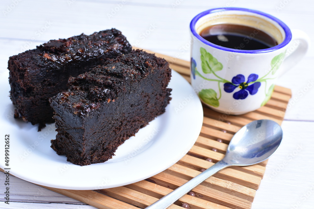Traditional black ponque, with raisins, red wine flavor accompanied by a cup of coffee on a wooden background Traditional black ponque, with raisins, red wine flavor accompanied by a cup of coffee on a wooden background
