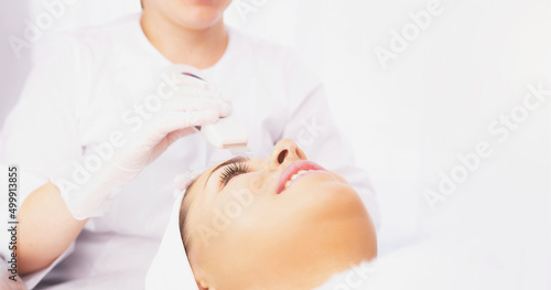 Cropped photo of cosmetologist's hands in white gloves doing ultrasonic peeling of woman's face in a clinic beauty salon.