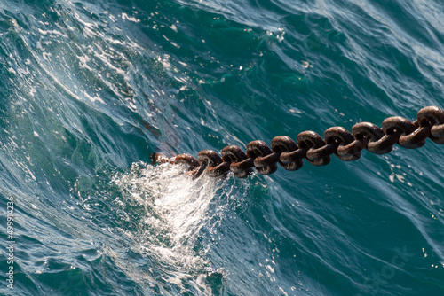 Anchor chain going dowm in the water with waves and splashes. photo