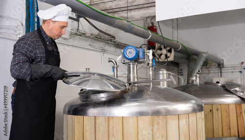 Focused skilled brewmaster opening lid of fermenter while checking process of craft beer production in workshop.. photo