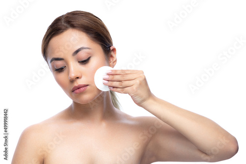 Close up portrait of a beautiful half naked woman with perfect, natural, clean and cosmetic skin and looking away. Taking off makeup with cotton wipe sponge or pads. Isolated over white background.