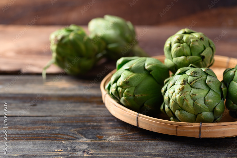 Green artichoke in bamboo basket on wooden background, Edible flower bud Green artichoke in bamboo basket on wooden background, Edible flower bud