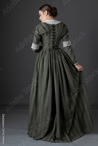 Fotografering A Victorian working class woman wearing a checked bodice and skirt and standing