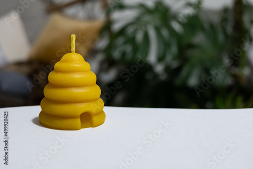 A beehive votive shaped beeswax candle is sitting on white paper with plants in the background. photo