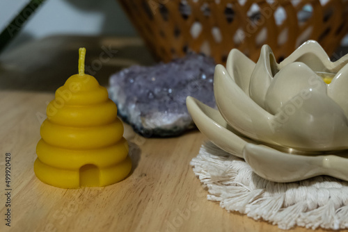 A beehive votive shaped beeswax candle is displayed next to a crystal and flower shaped candle holder. photo