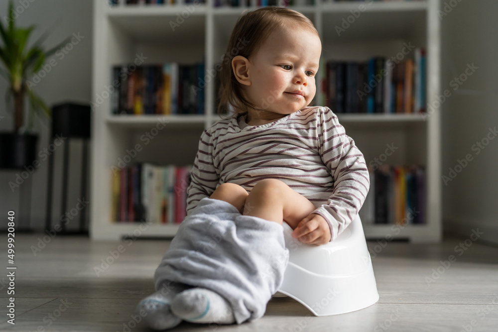One small caucasian baby girl one year old sitting on the children's potty at home on the floor in day full length front view copy space One small caucasian baby girl one year old sitting on the children's potty at home on the floor in day full length front view copy space