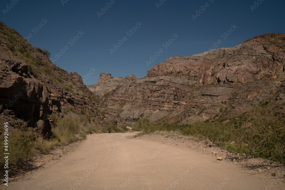 Travel. View of the dirt road across the arid desert and colorful rock formations.