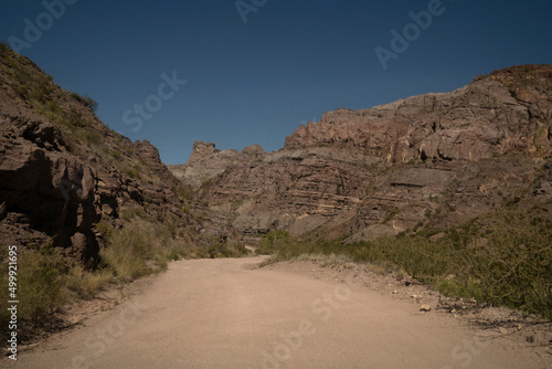 Travel. View of the dirt road across the arid desert and colorful rock formations.