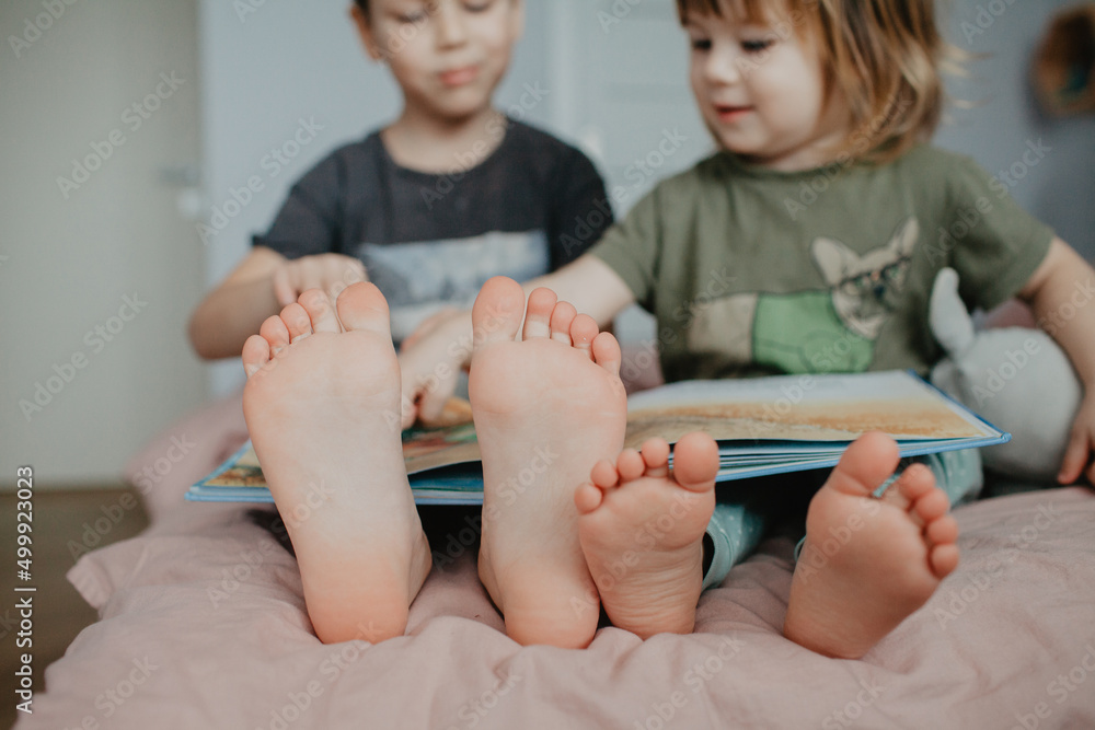 Big brother and little sister holding bare feet close up to camera