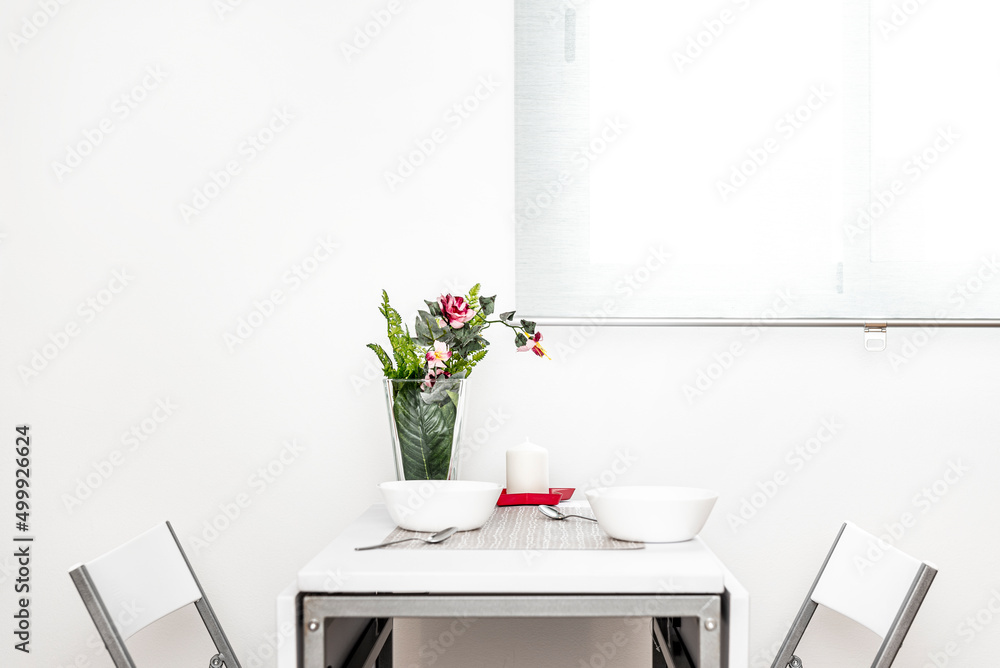 Fototapeta premium Small white folding dining table with matching chairs, tableware set with artificial plant vase