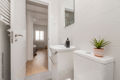 Bathroom with frameless square mirror  white porcelain sink on gloss white wooden cabinet  white heated towel rail behind the wall and decorative plant