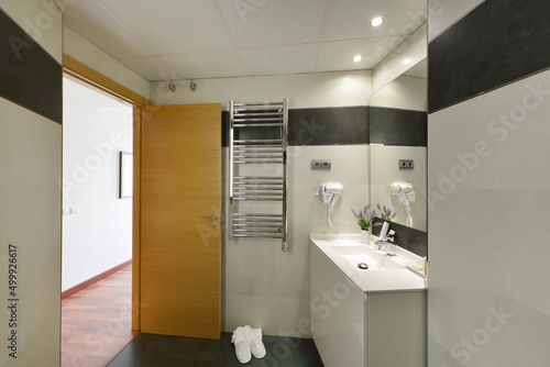 Bathroom with chrome heated towel rail  frameless mirror and white bath slippers