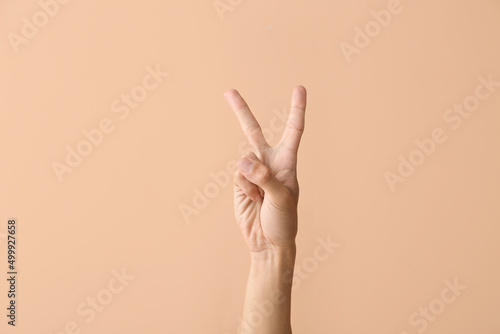 Young male hand showing victory gesture on color background