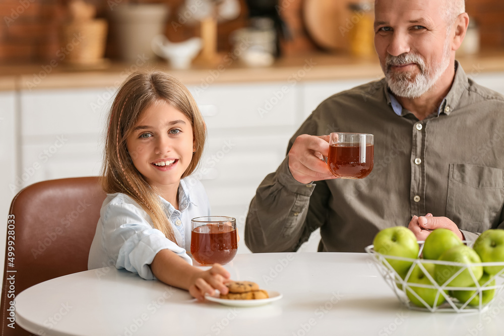 Little girl with cookies and her grandfather drinking tea in kitchen
