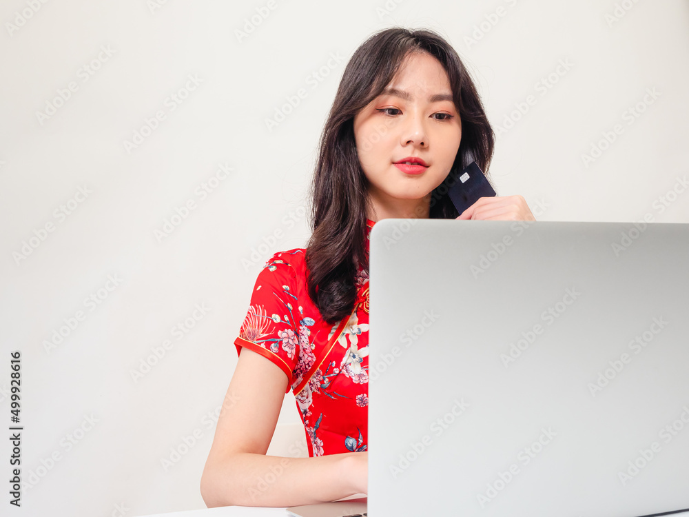 Asian young woman wearing traditional cheongsam qipao dress using laptop and credit card shopping online, e-commerce concept isolated on white background. Asian young woman wearing traditional cheongsam qipao dress using laptop and credit card shopping online, e-commerce concept isolated on white background.