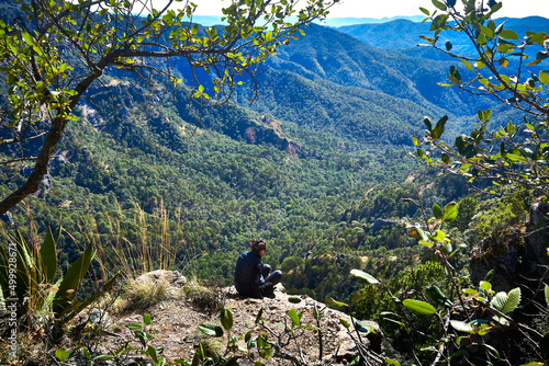 mujer joven sentada frente a un valle con grandes montañas y un hermoso bosque en un día soleado en mexiquillo Durango  © Alex Borderline