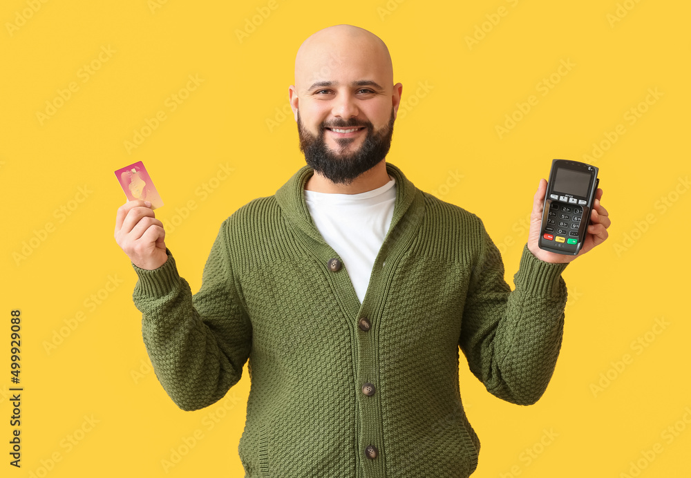 Bald man with payment terminal and credit card on yellow background Bald man with payment terminal and credit card on yellow background