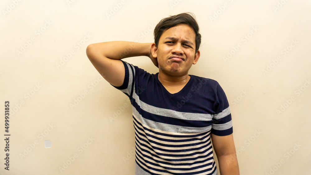 Confused and bewildered face expression with hand behind head of young Asian Malay man with strips t-shirt. Confused and bewildered face expression with hand behind head of young Asian Malay man with strips t-shirt.