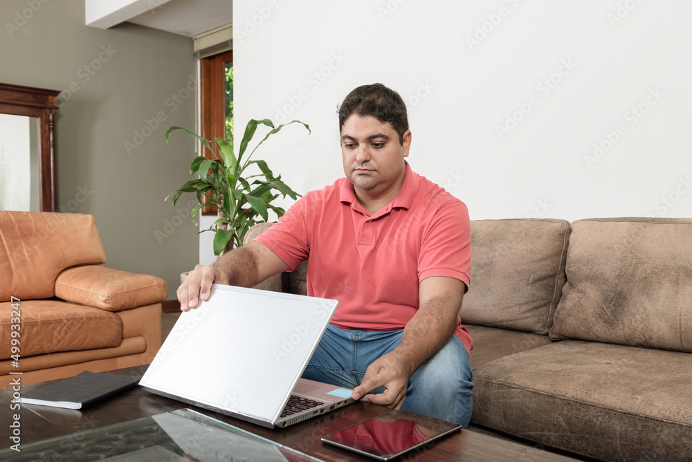Homem jovem brasileiro trabalhando em casa com laptop