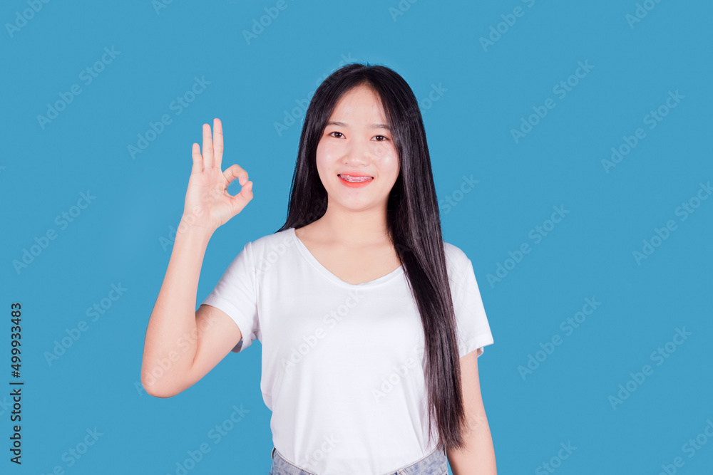 Beautiful Asian woman with long dark hair wear white t-shirt top showing ok-sign on blue background Beautiful Asian woman with long dark hair wear white t-shirt top showing ok-sign on blue background
