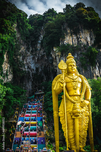 Close up portrait of Lord Murugan Statue in foothills of limestone outcrop, Batu Caves Gombak. Golden Buddha Statue at the entrance of Batu Cave.