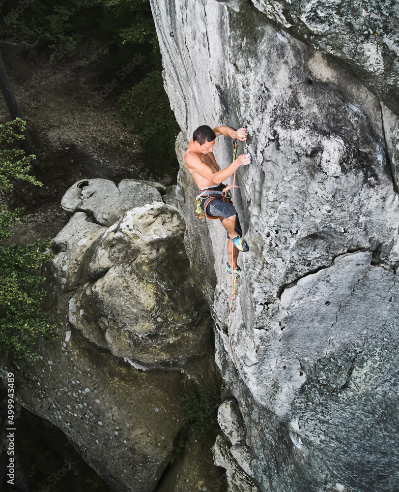 Young man climber climbing difficult route on a high rock with rope