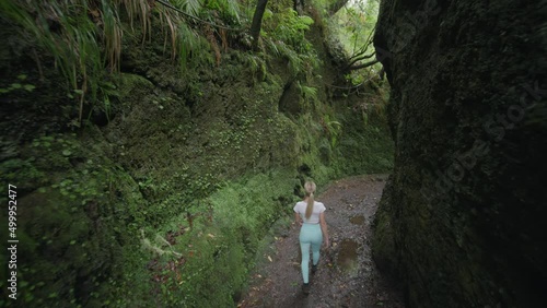 Woman walking through moss covered rock wall canyon in primeval forest photo