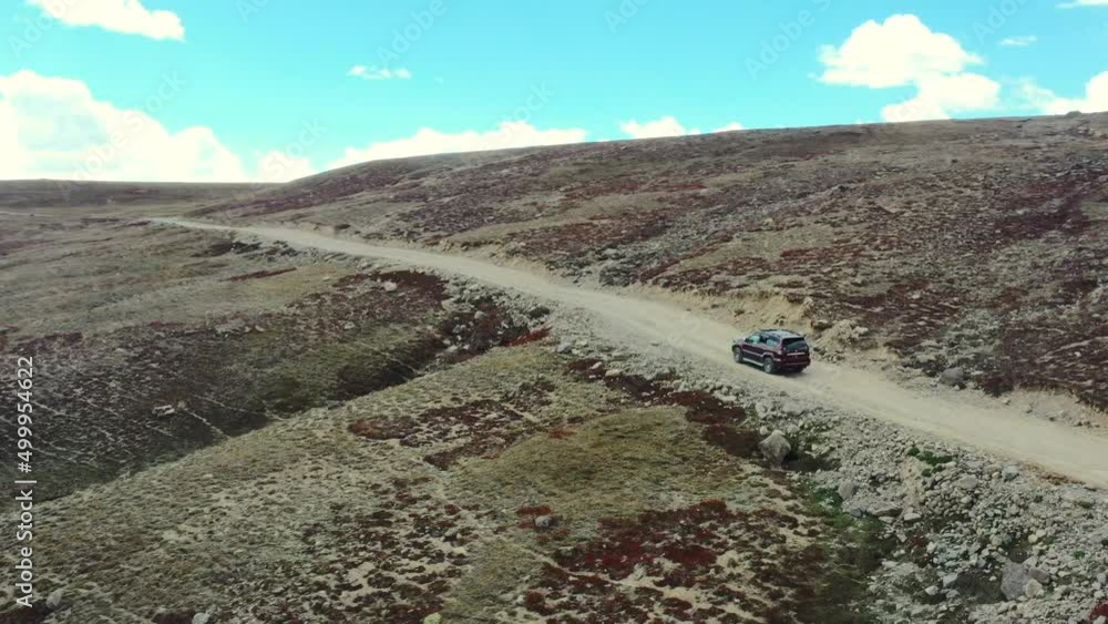 Aerial drone of a red suv driving up a hill slowly on a dirt road path in the high-altitude alpine plain and mountains of Deosai National Park located between Skardu and Astore Valley in Pakistan Aerial drone of a red suv driving up a hill slowly on a dirt road path in the high-altitude alpine plain and mountains of Deosai National Park located between Skardu and Astore Valley in Pakistan