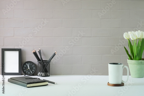 Stylish workplace with empty picture frame, coffee cup, notebook and tulips in a pot. Copy space for advertise text or information content.