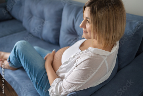 pregnant girl in a white shirt and blue jeans sits on a gray sofa