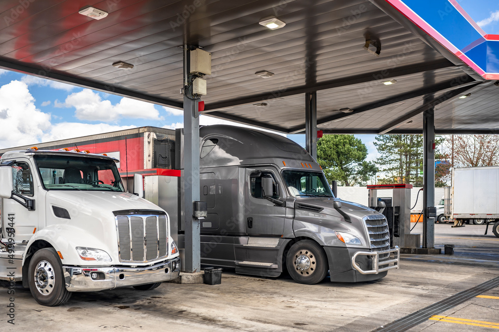 Day cab big rig semi truck and long haul gray semi truck with dry van semi trailer refuel tanks with diesel at a gas station on the territory of the truck stop