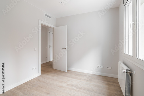 Empty room with door, window, and heating radiator in a white interior house