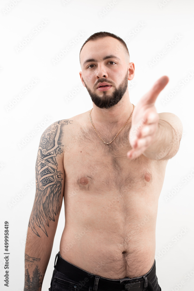 Portrait of young confident bearded man with short dark hair wearing black jeans, golden chain with bare torso standing. Portrait of young confident bearded man with short dark hair wearing black jeans, golden chain with bare torso standing.