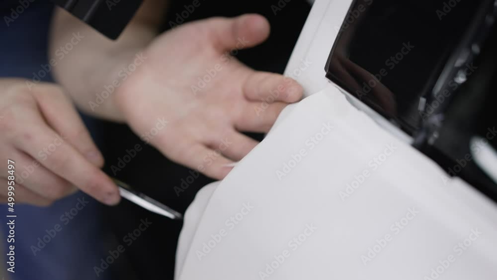Protective white car film. Auto detailing. Professional worker installs paint protection. Retrofitting the car with a continuous protective film. Protective white car film. Auto detailing. Professional worker installs paint protection. Retrofitting the car with a continuous protective film.