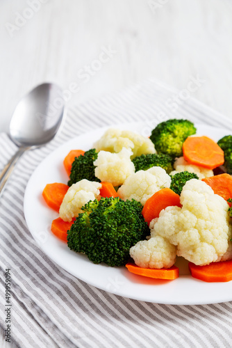 Mixed Organic Steamed Vegetables (Carrots, Broccoli and Cauliflower) on a Plate on a white wooden background, side view.