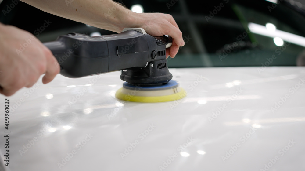 Car detailing and polishing concept. Hands of professional car service male worker, with orbital polisher, polishing white luxury car hood in auto repair shop. Car hood polishing. Car detailing and polishing concept. Hands of professional car service male worker, with orbital polisher, polishing white luxury car hood in auto repair shop. Car hood polishing.