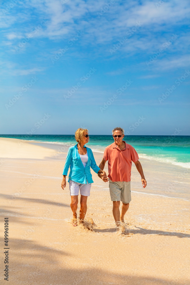 Retired couple walking together on beach holding hands Retired couple walking together on beach holding hands