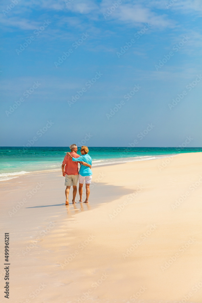 Travel retired couple walking barefoot on sandy beach