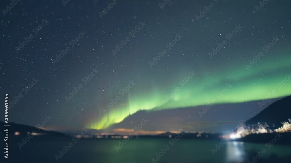Northern lights above the fjord. Street and car lights flash in the background. Clouds in the sky. Timelapse. Northern lights above the fjord. Street and car lights flash in the background. Clouds in the sky. Timelapse.
