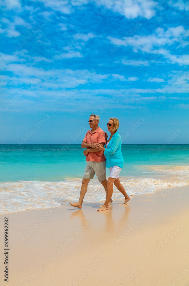 Retired male and female walking by turquoise ocean Retired male and female walking by turquoise ocean