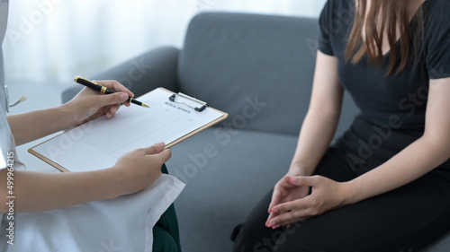 Professional physician wearing white coat talking with patient and signing medical paper at appointment visit in clinic.