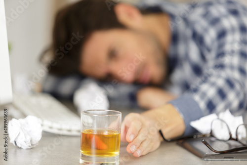 man slumped across desk reaching for alcoholic drink