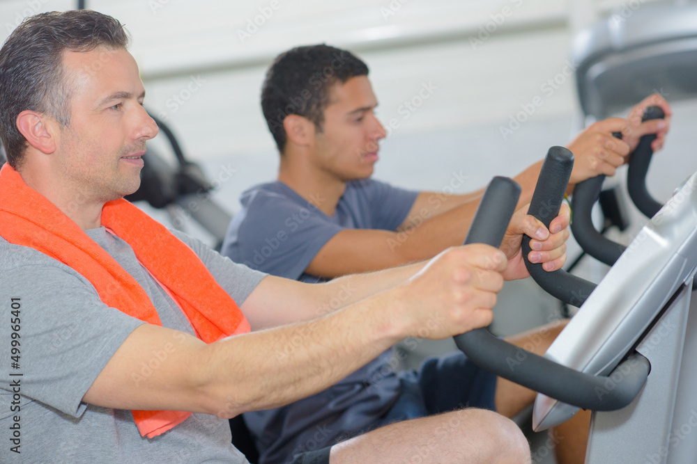 Two men on exercise machines Two men on exercise machines