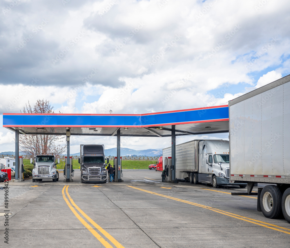 Truck drivers refuel tanks of different big rigs semi trucks at the truck stop gas station